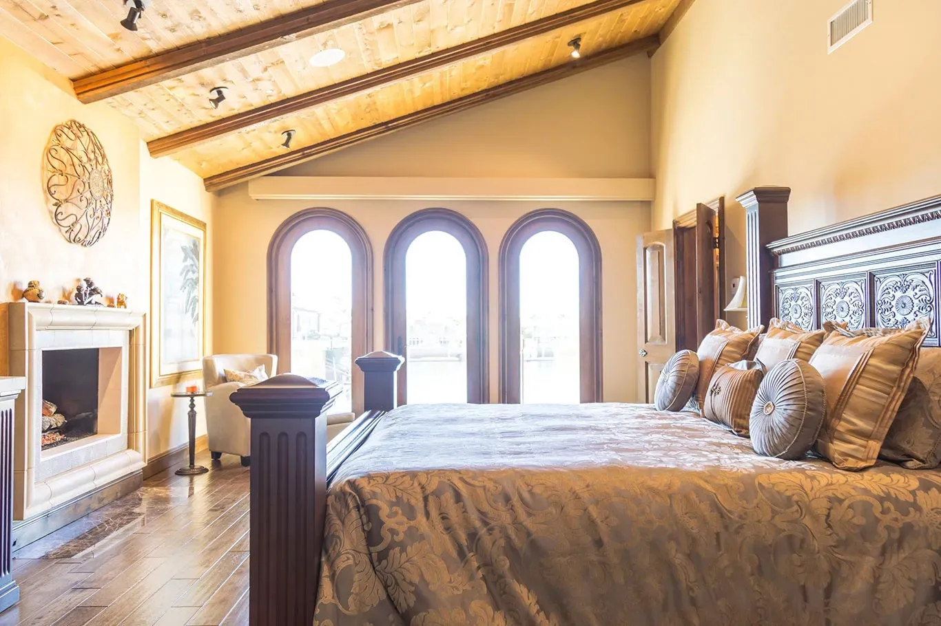 A bedroom with a king size bed , fireplace , and arched windows.