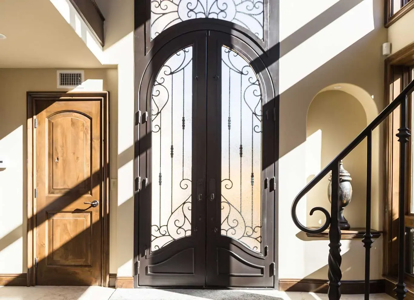 A door with a wrought iron design is in a hallway next to a staircase.