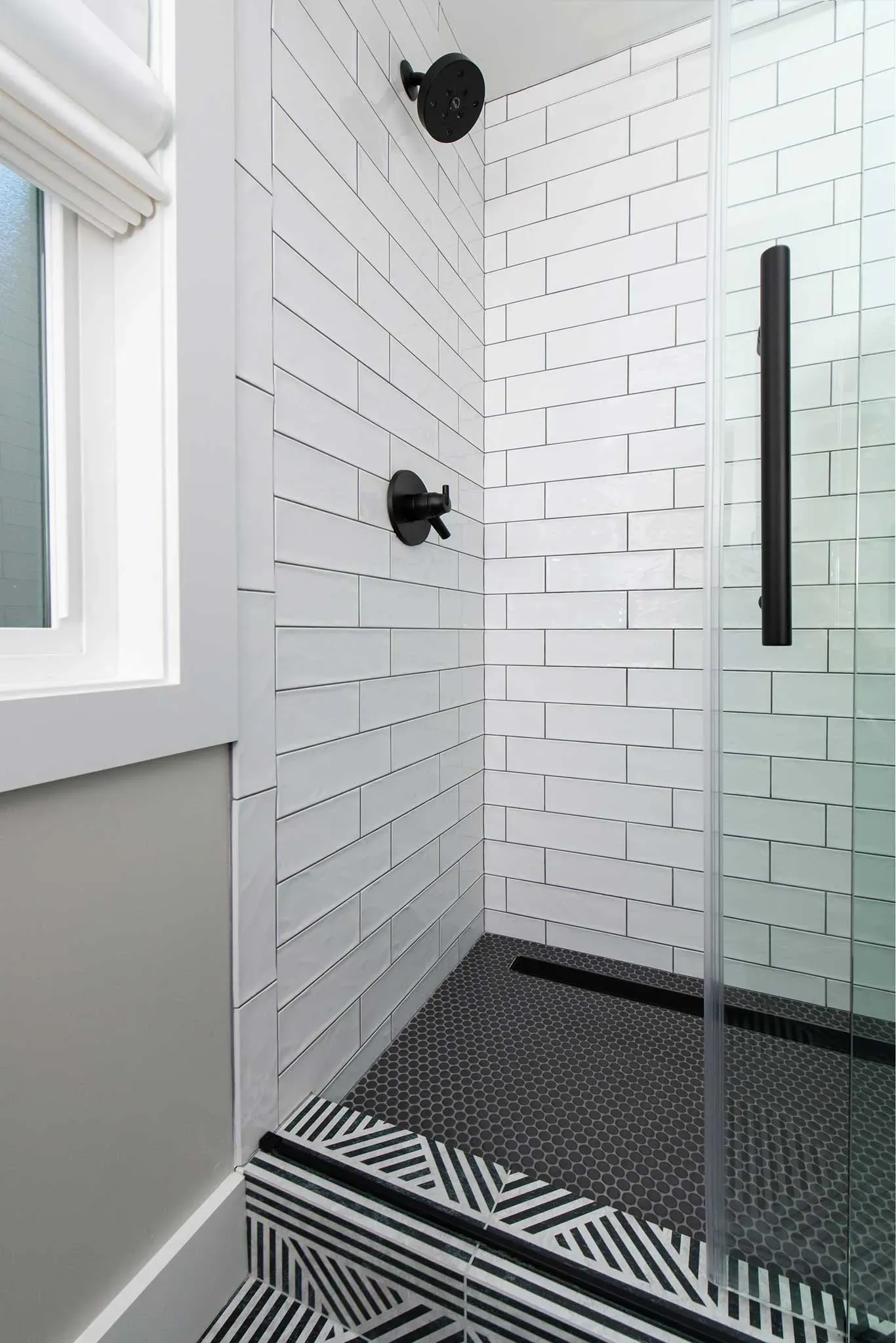A bathroom with a walk in shower with a black and white tile floor.