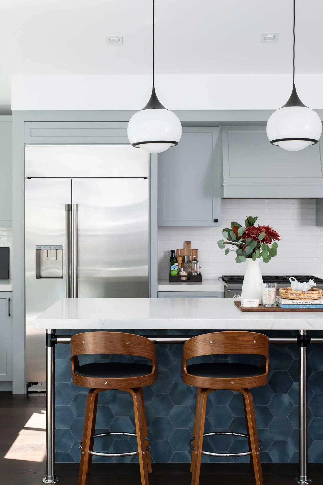 A kitchen with a large island , stools , a refrigerator and a vase of flowers on the counter.