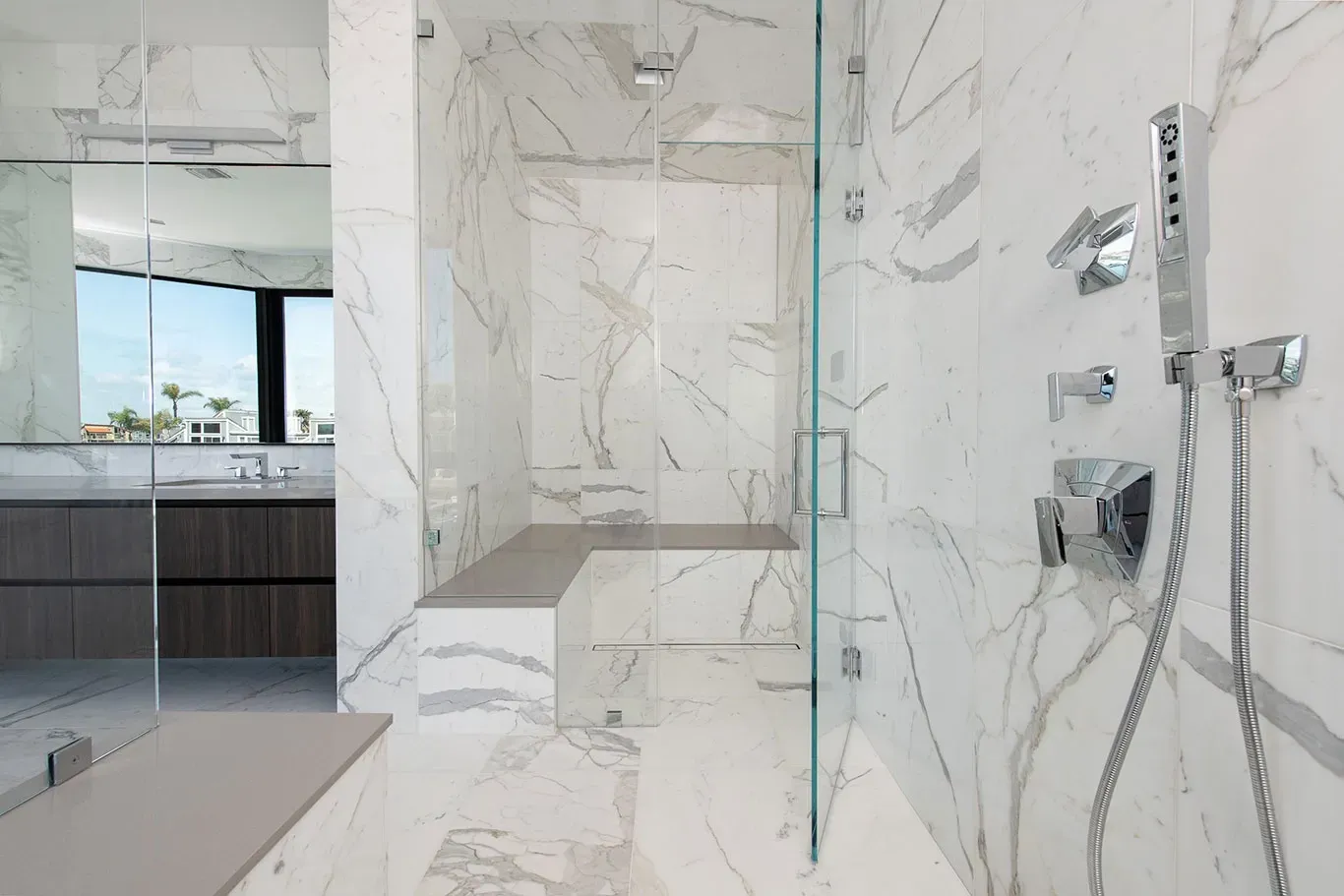 A bathroom with marble walls and a walk in shower with a glass door.