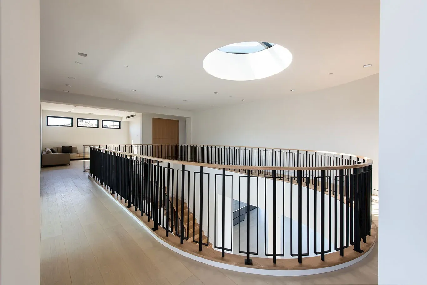 A curved staircase with a black railing and a skylight in the ceiling.