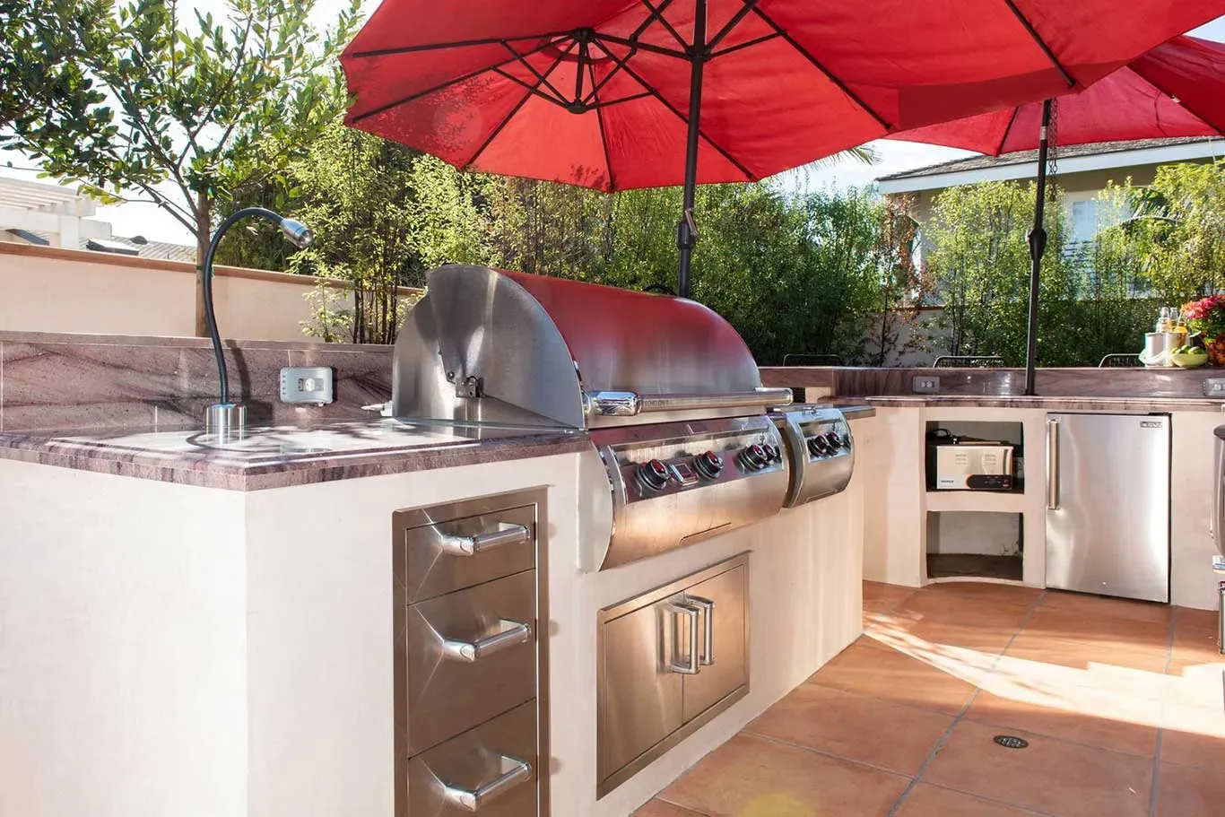 An outdoor kitchen with a grill and red umbrellas.