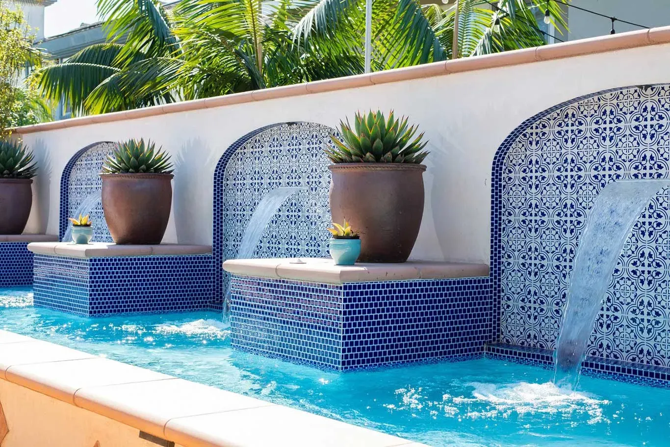 A swimming pool with a waterfall and potted plants