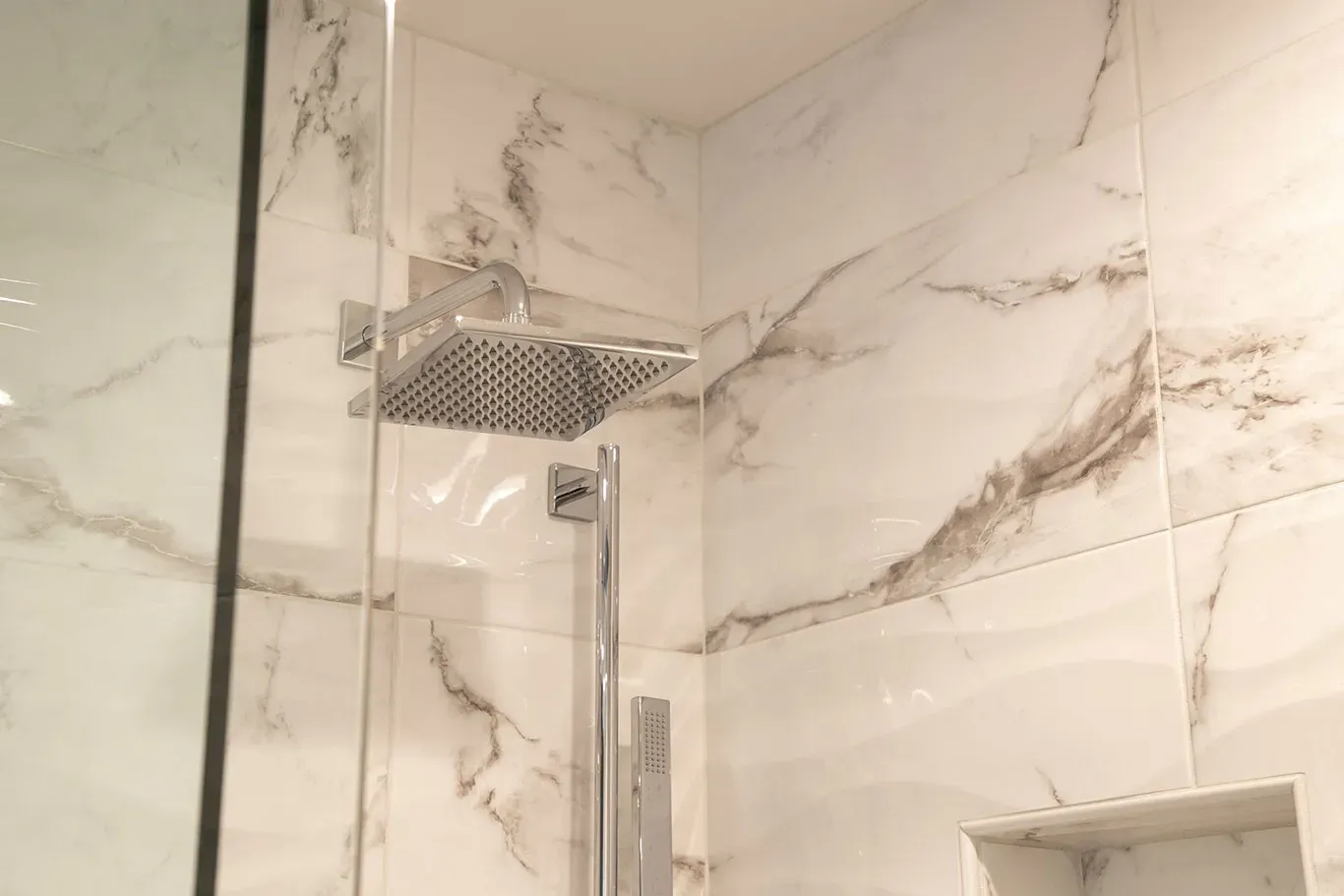 A bathroom with marble tiles and a shower head.