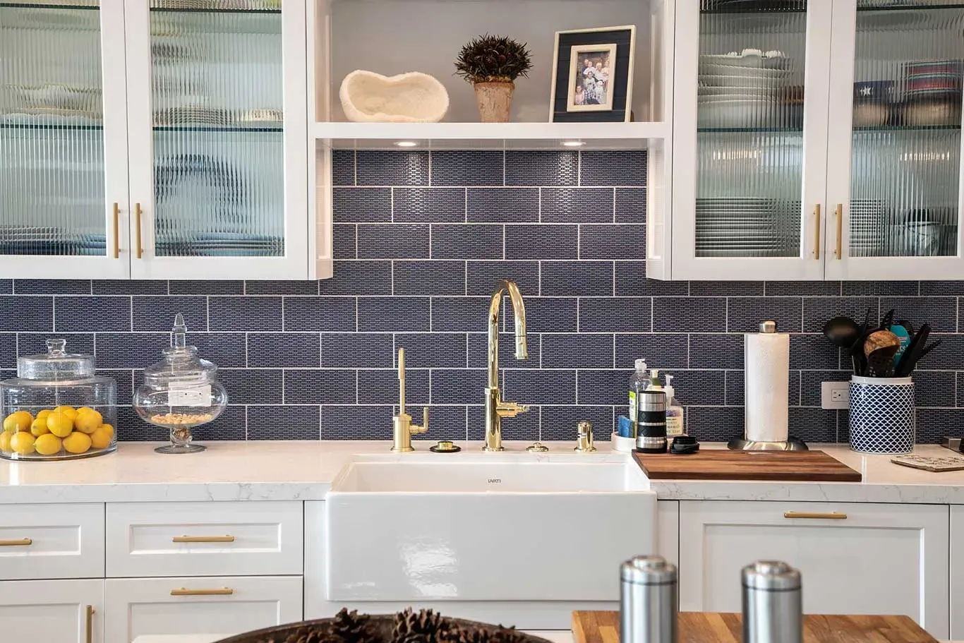 A kitchen with white cabinets , a sink , and a subway tile wall.