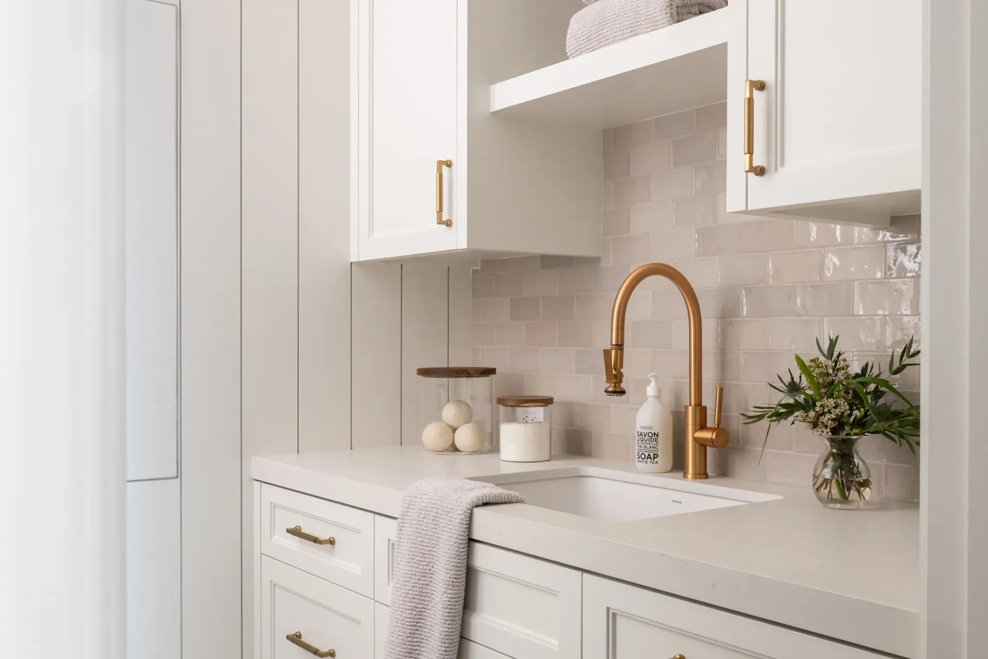A laundry room with white cabinets , a sink , and a copper faucet.