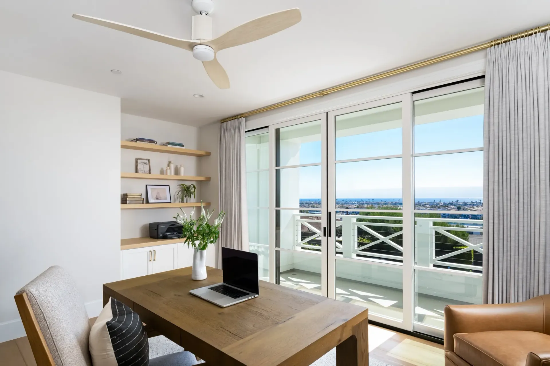There is a desk with a laptop on it and a ceiling fan in the room.