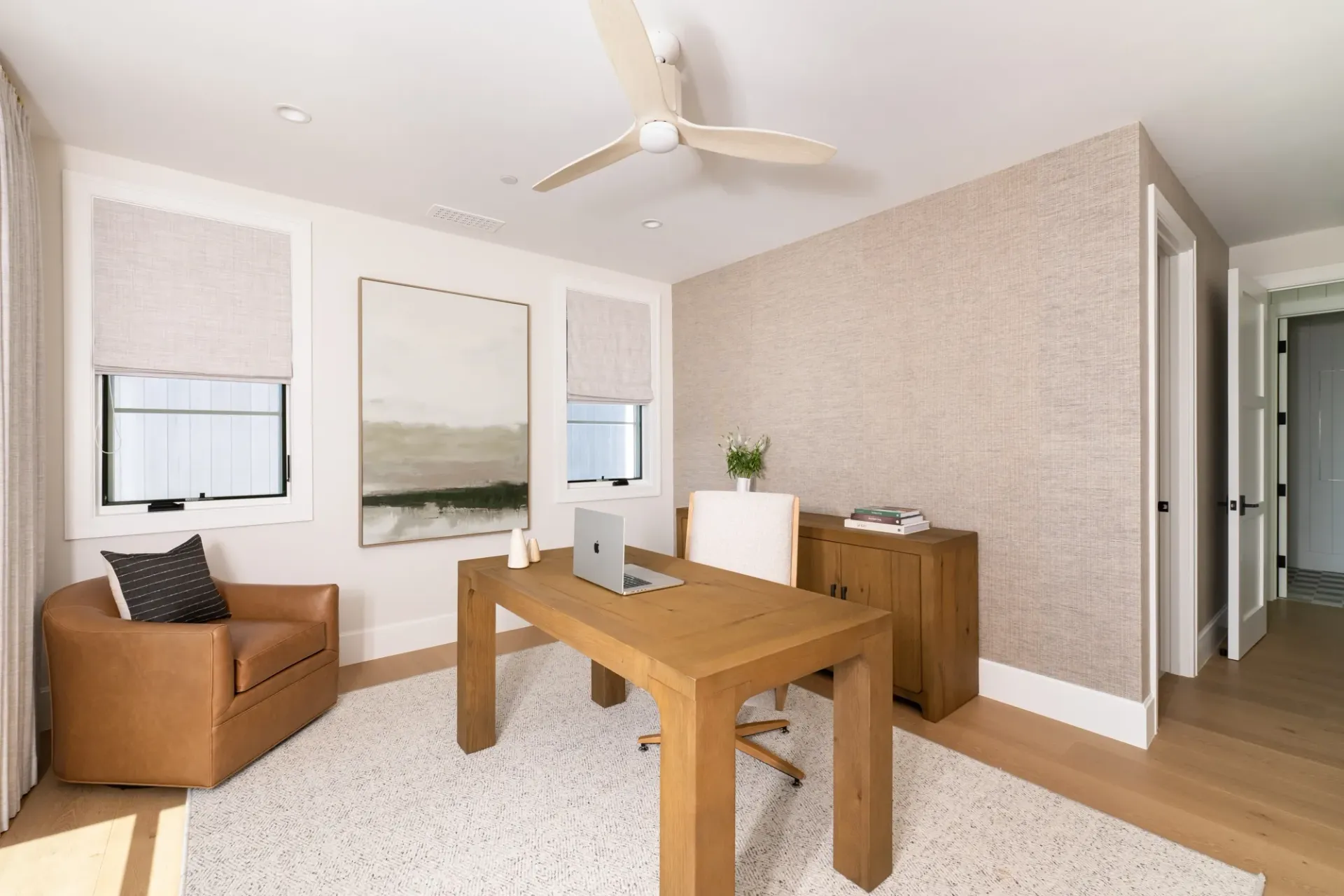 A home office with a wooden desk , chair , and ceiling fan.