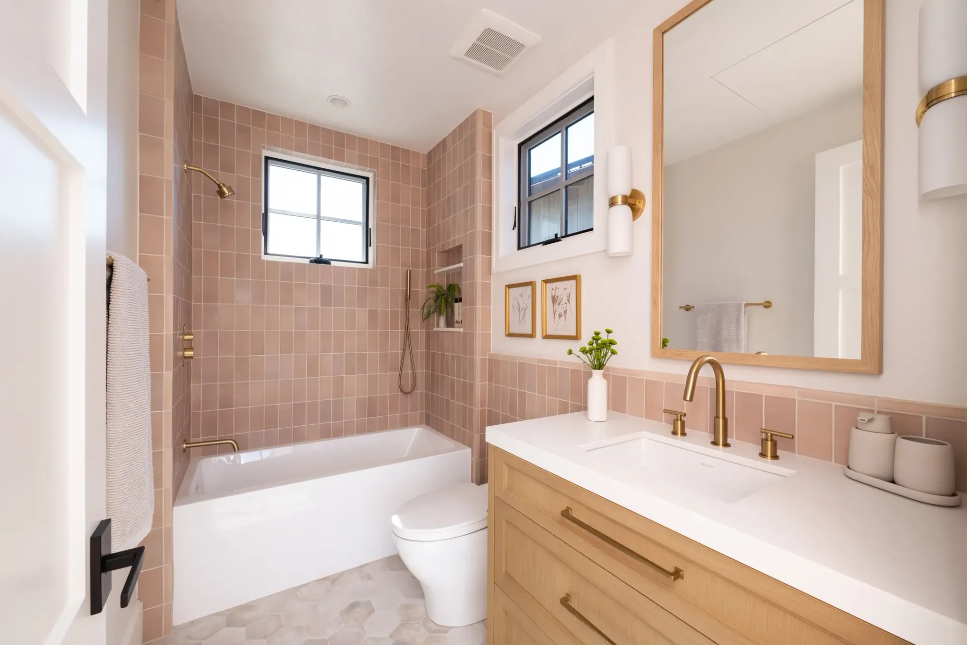 A bathroom with pink tiles , a sink , a toilet , and a window.