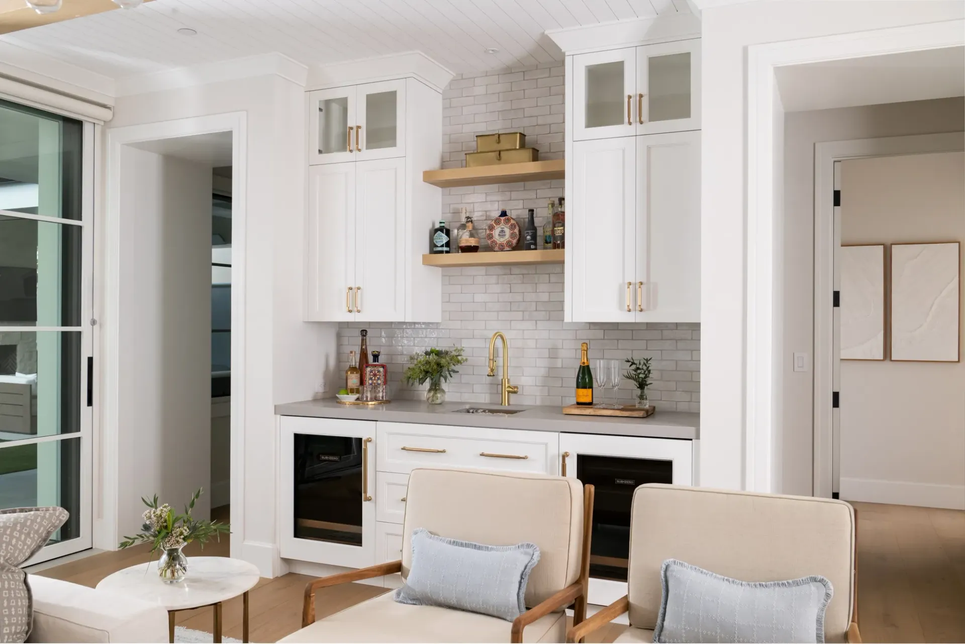 A living room with white cabinets , chairs , a table and a bar.
