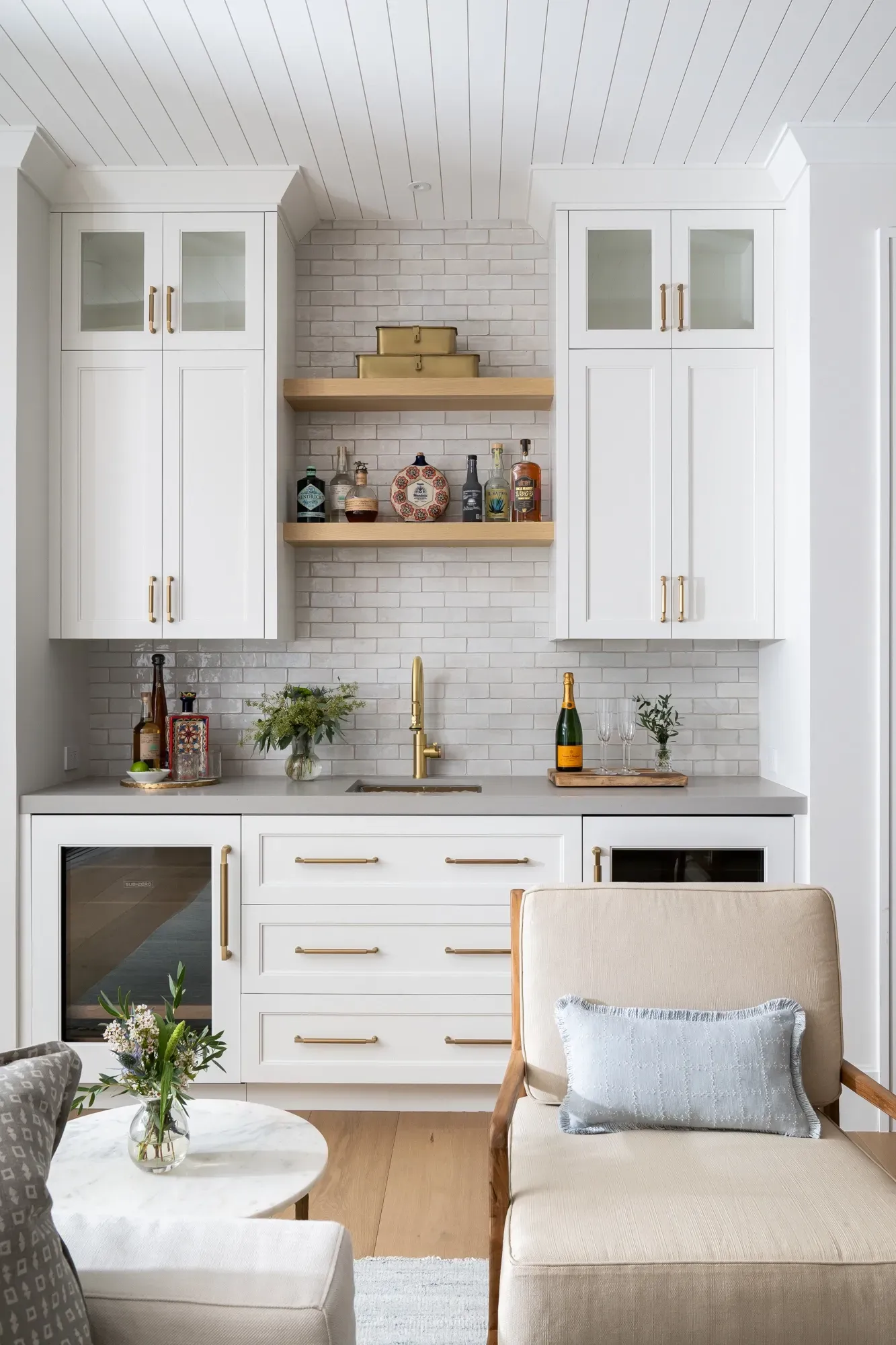 A living room with white cabinets , a chair , a table and a refrigerator.