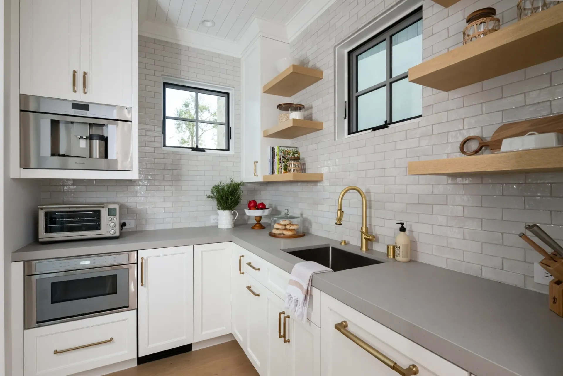 A kitchen with white cabinets , a sink , a microwave , and a window.