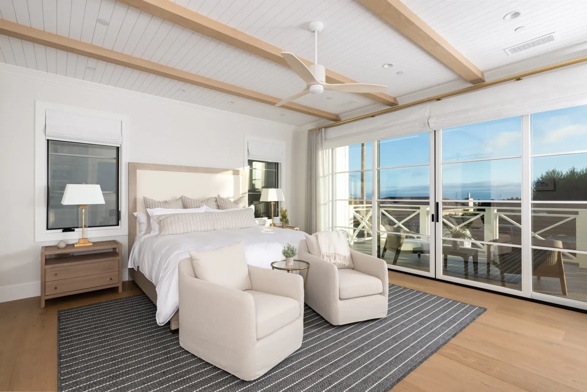 A bedroom with a large bed , two chairs , a rug and a ceiling fan.