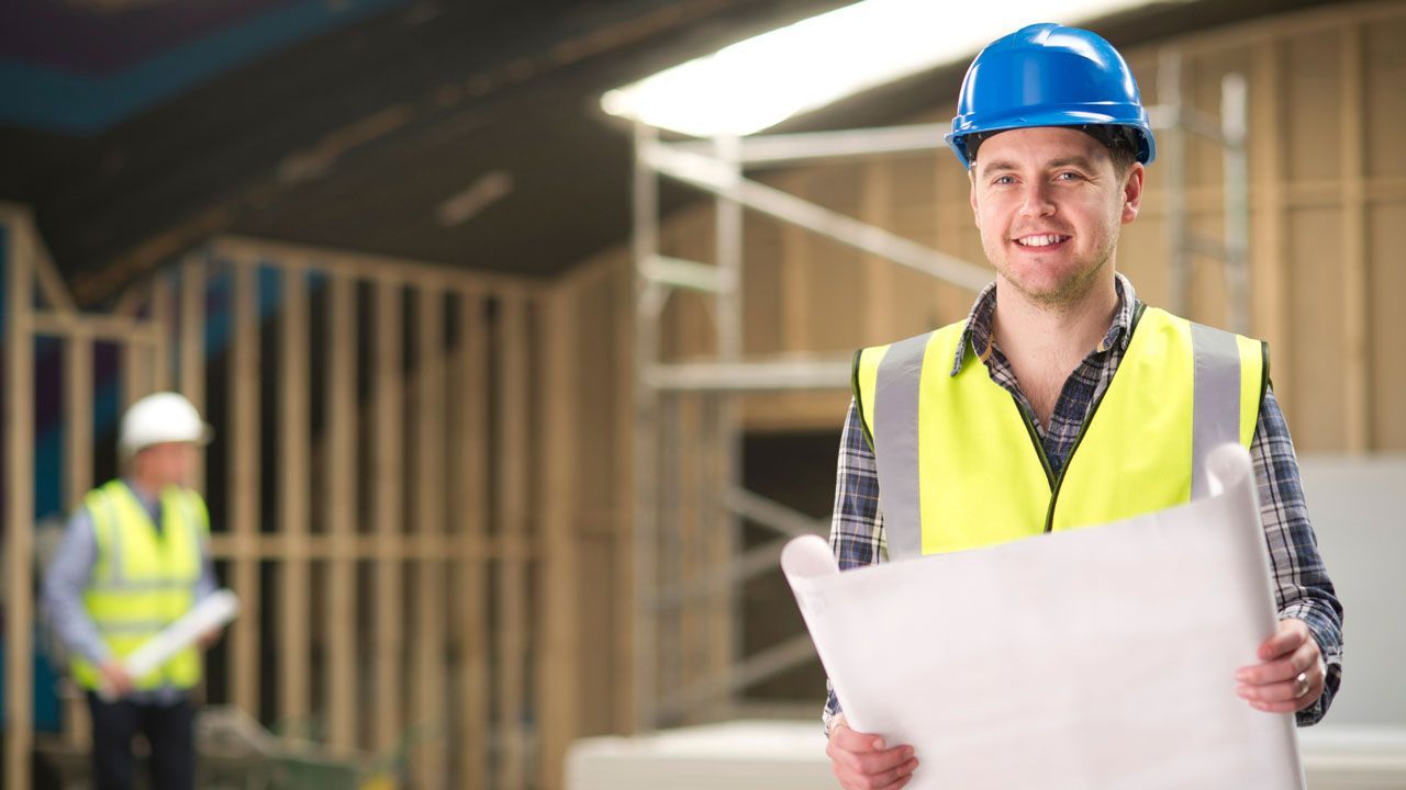 A construction worker is holding a blueprint in a construction site.