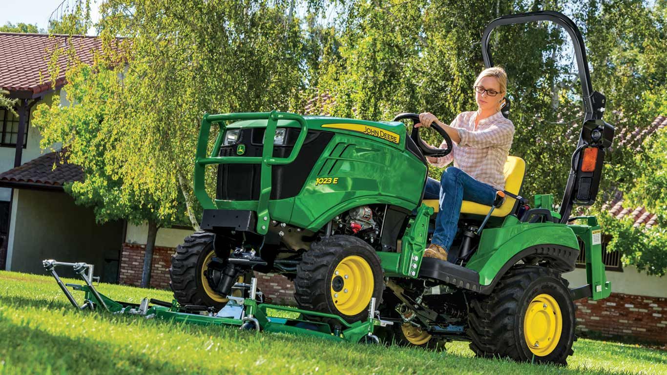 A woman is riding a john deere lawn mower on a lush green lawn.
