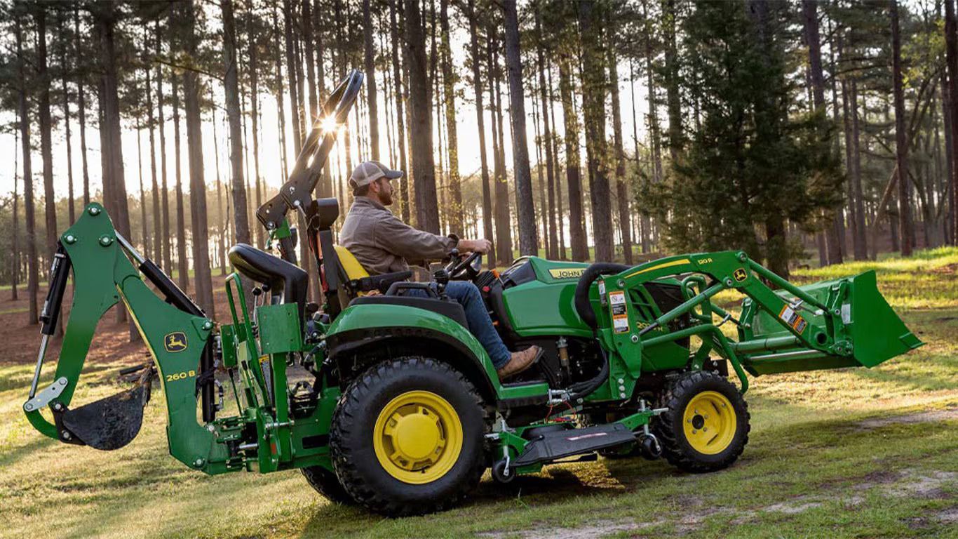 A man is driving a green tractor with a backhoe attached to it.