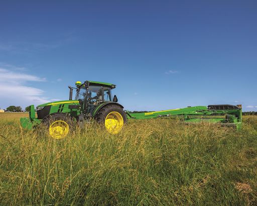 A green and yellow John Deere utility tractor is driving through a grassy field.