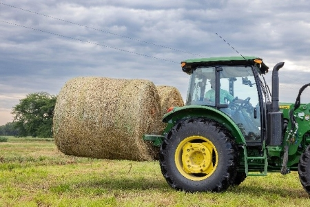 A green John Deere tractor is carrying bales of hay in a field.