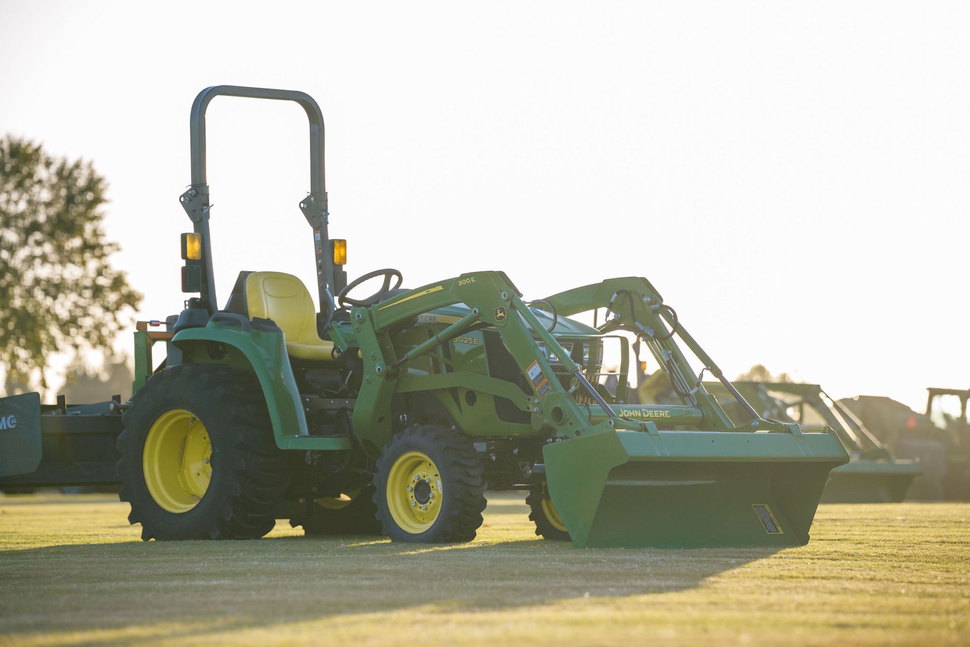 A 3025e tractor is parked in front of a John Deere Lasseter Tractor dealership sign.