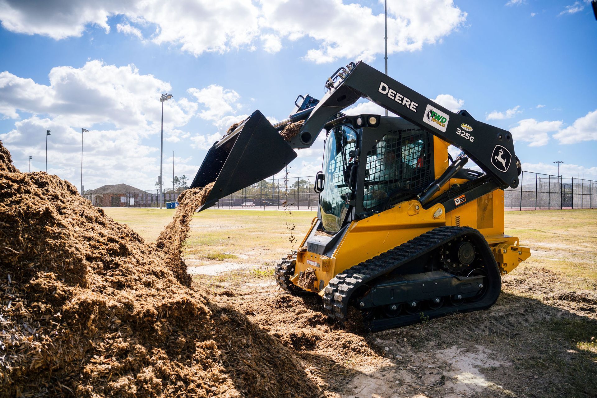 A compact track loader is scooping dirt from a pile in a field.