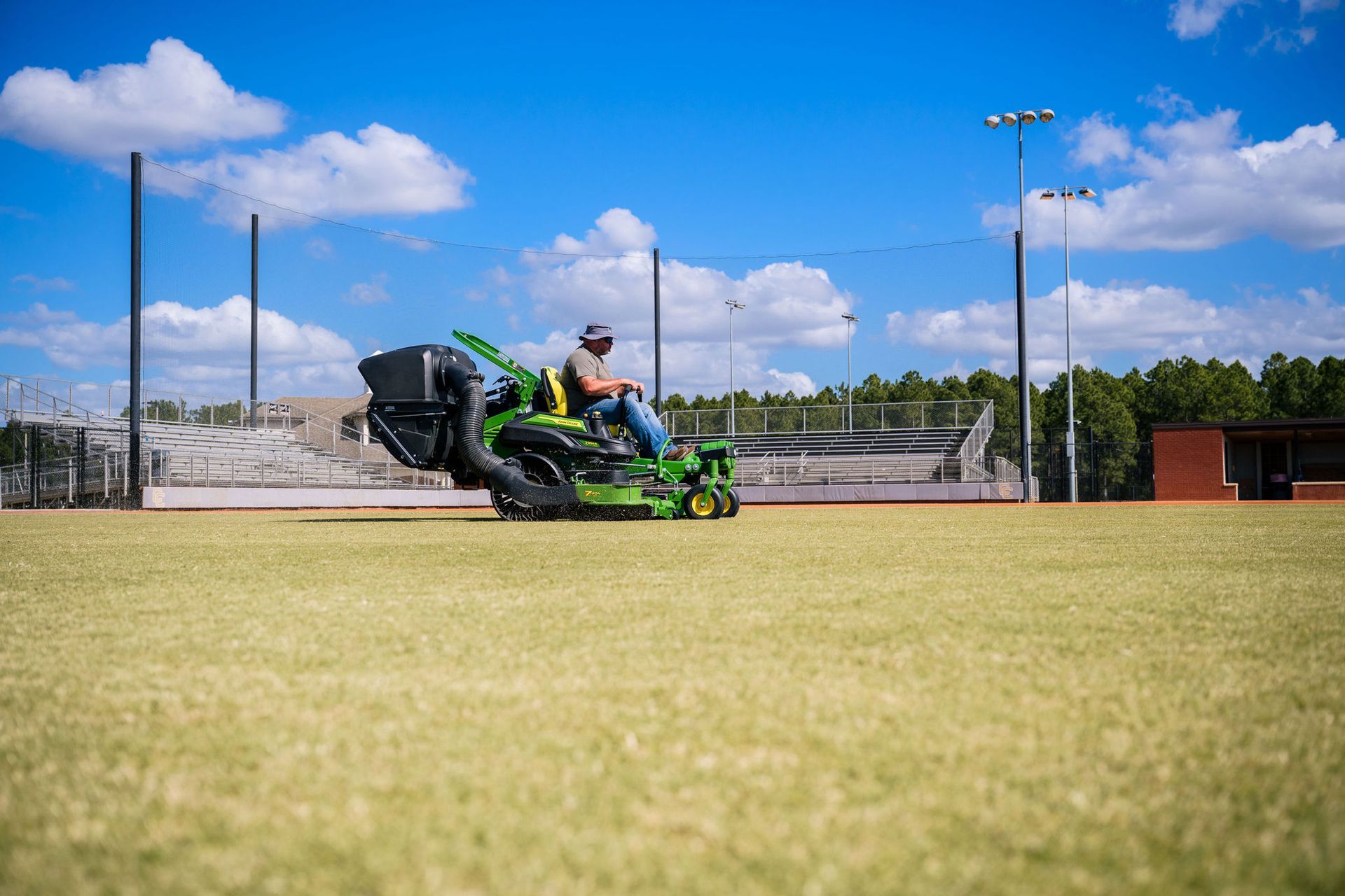 A man is riding a mower on a baseball field.