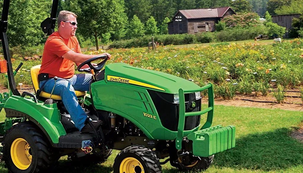 A man is riding a john deere tractor in a field.