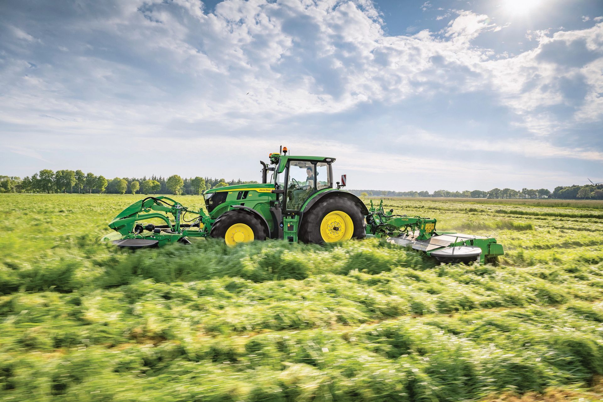 A green John Deere tractor is cutting grass in a field.