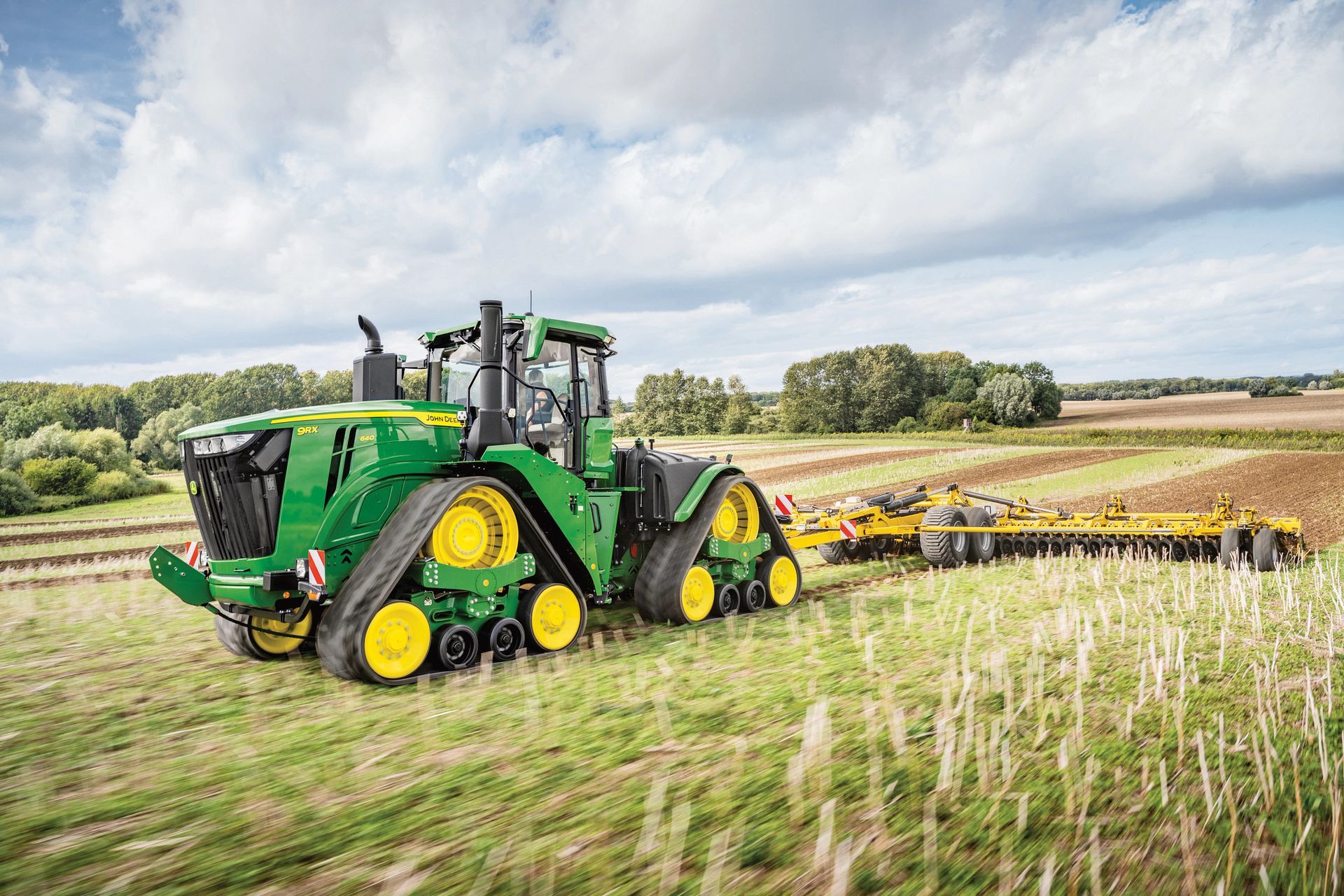A green and yellow john deere tractor is plowing a field.