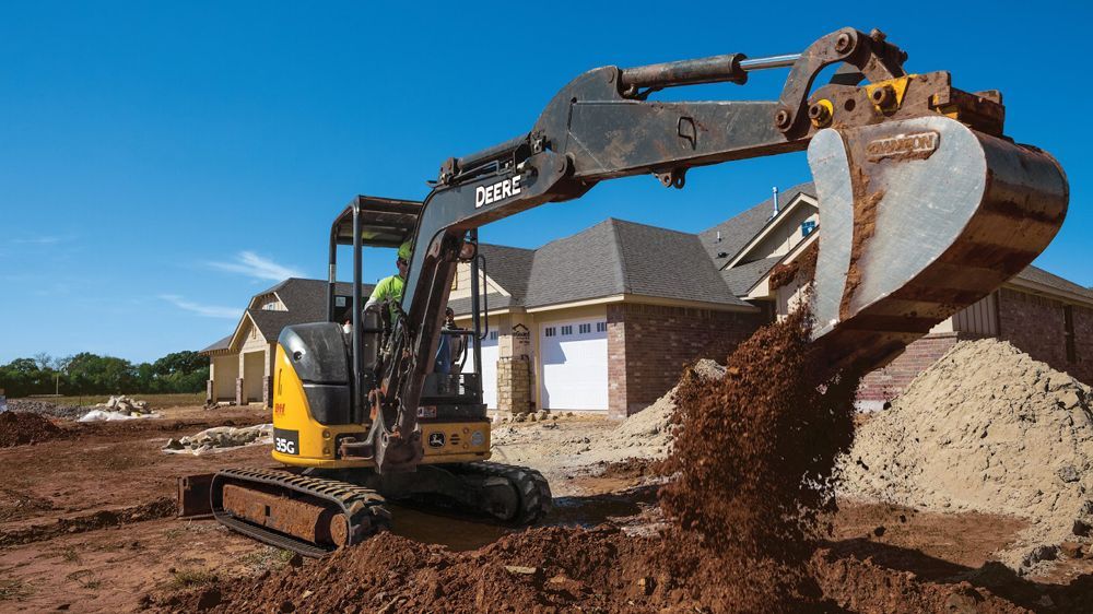 An excavator is digging a hole in the dirt in front of a house.