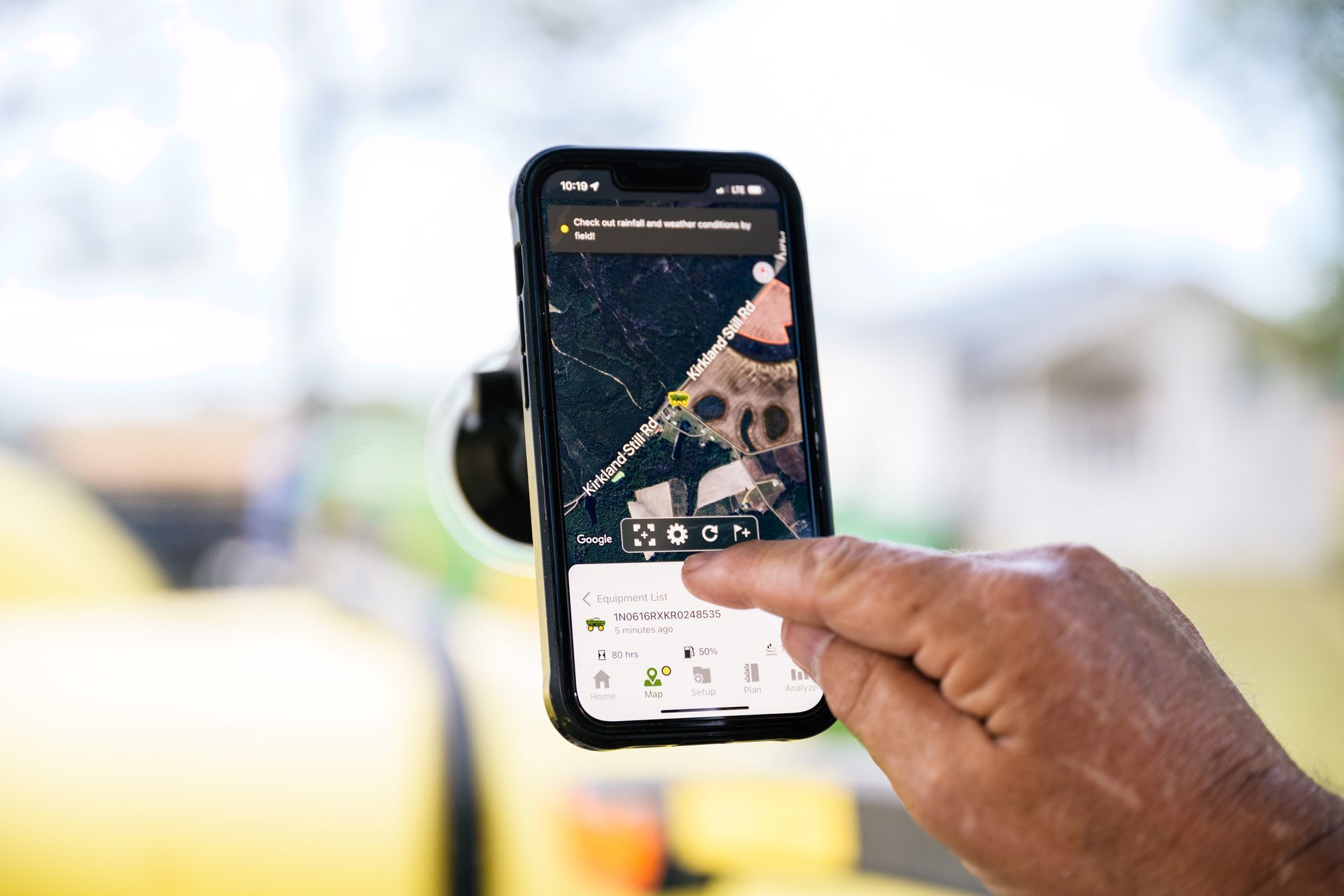 A person is pointing at a phone that is mounted against glass.