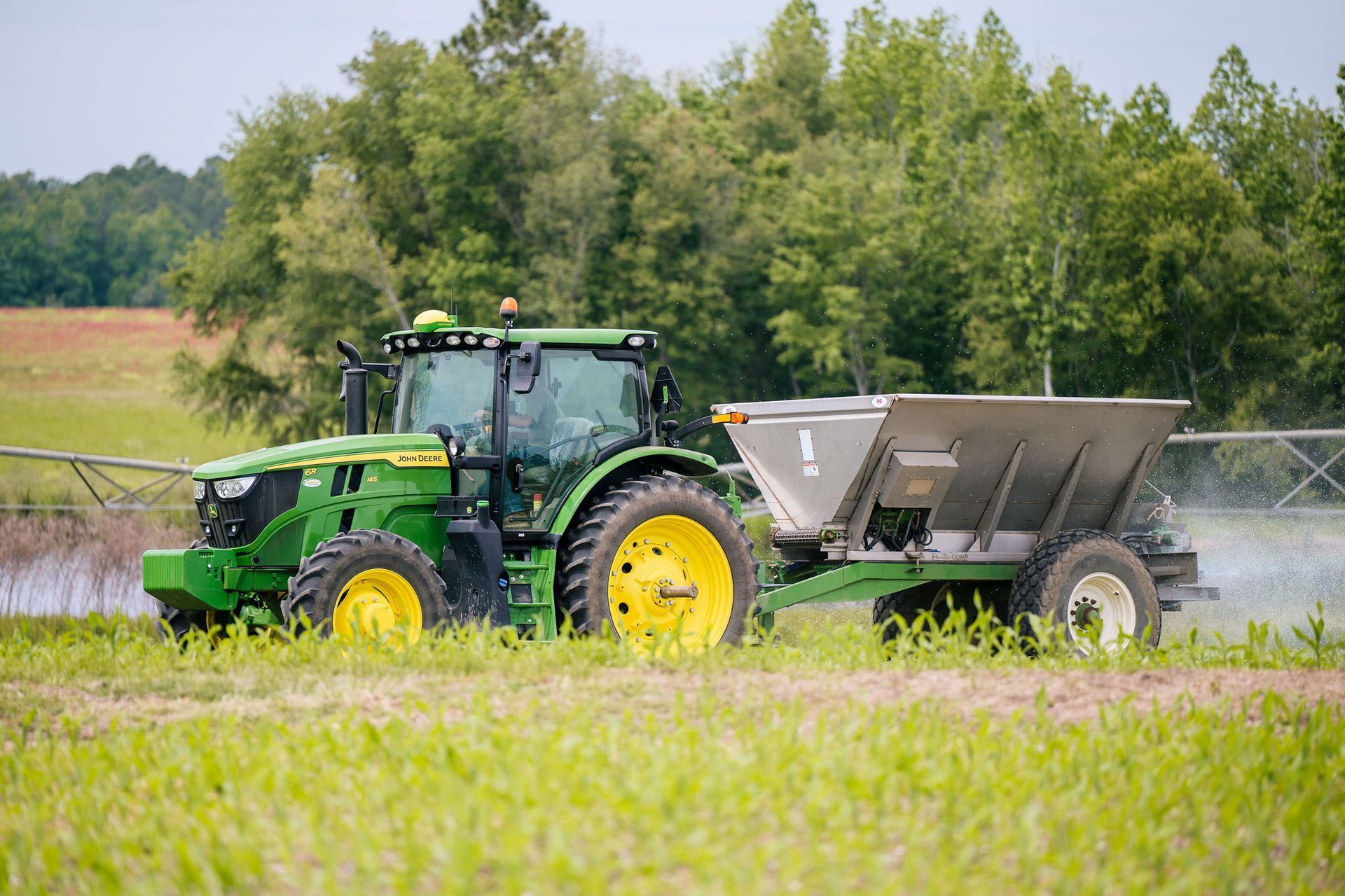 A green John Deere tractor is carrying a bale of hay in a field.