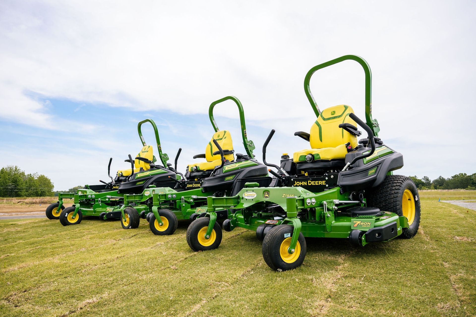 A row of john deere mowers are parked in a grassy field.