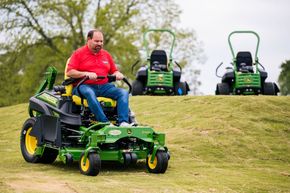 A man is riding a John Deere commercial mower on a lush green lawn.