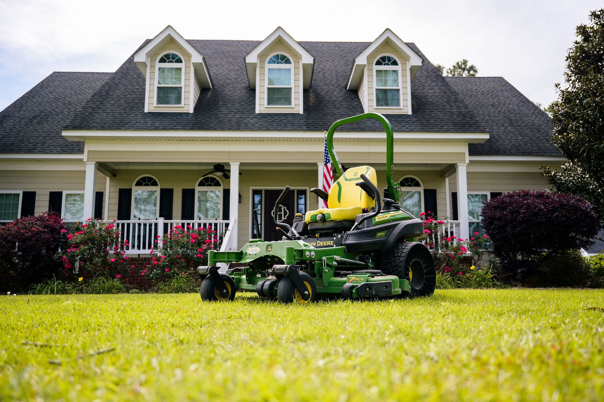A green John Deere mower is parked in front of a large house.