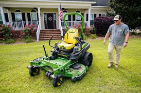 A man is riding a John Deere lawn mower on a lush green lawn.