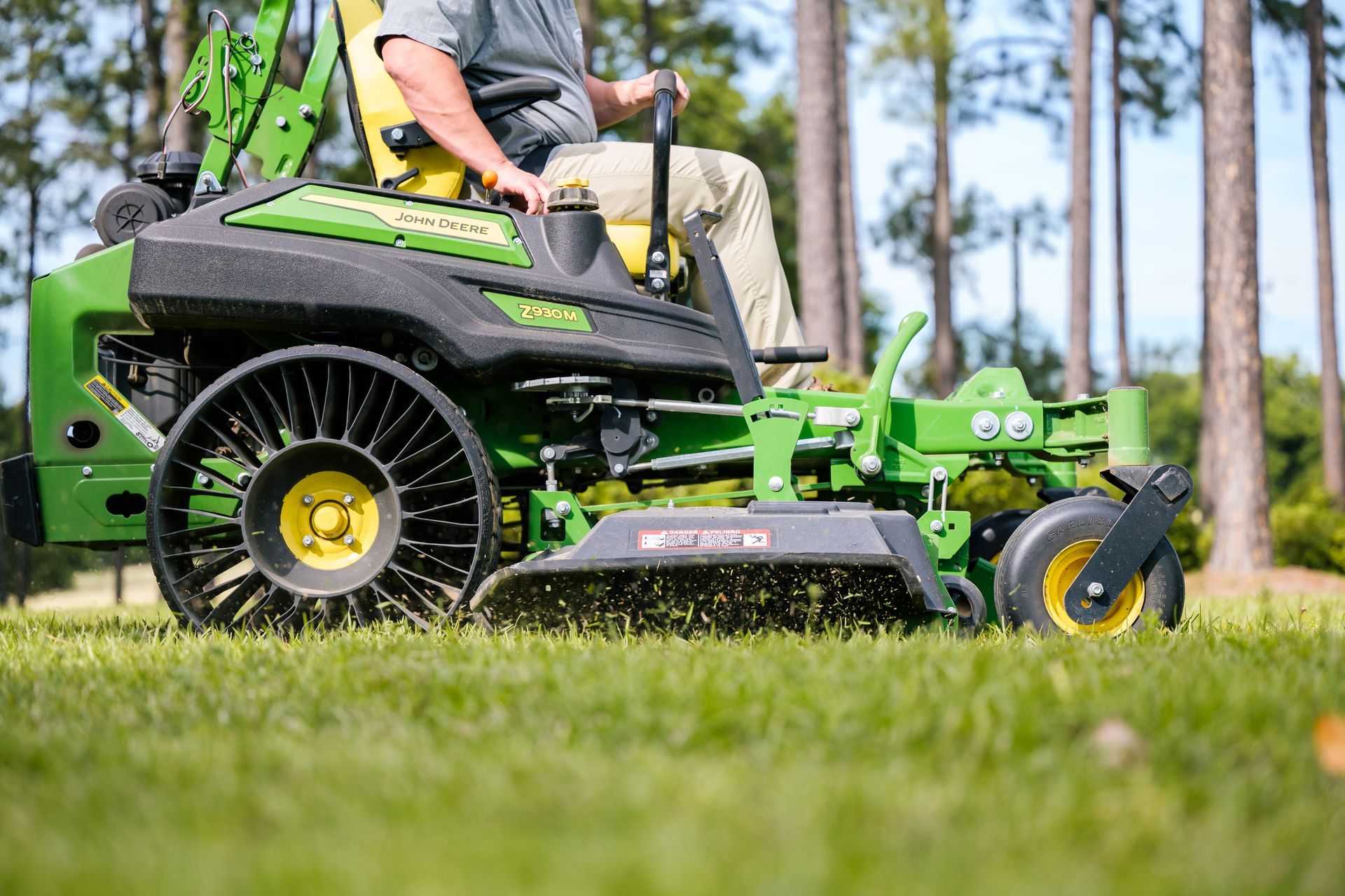 A man is riding a zero turn lawn mower on a lush green field.