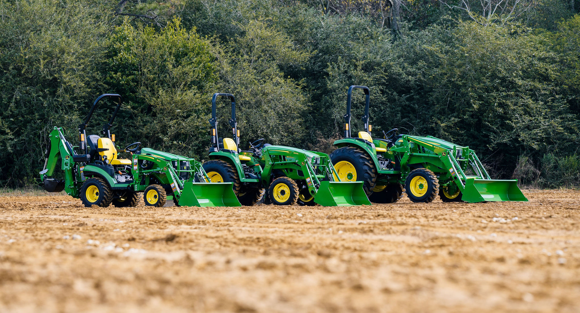 A row of john deere tractors are parked in a dirt field.