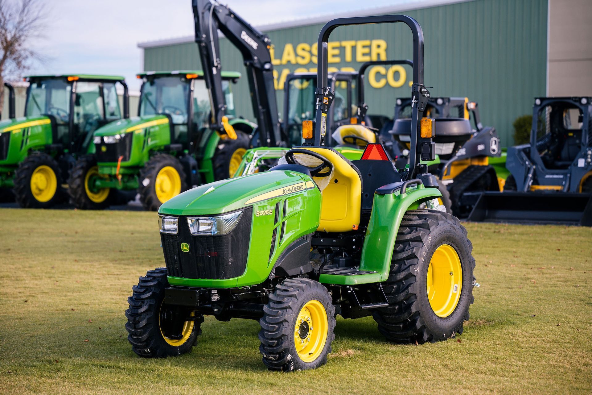 A green and yellow 3025e tractor is parked in front of a building.