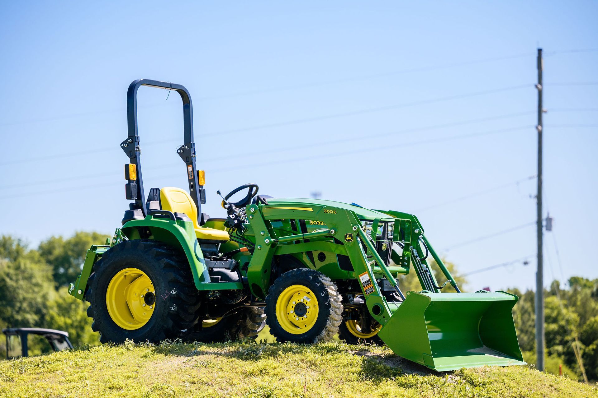 A green tractor with a bucket attached to it is parked on top of a grassy hill.