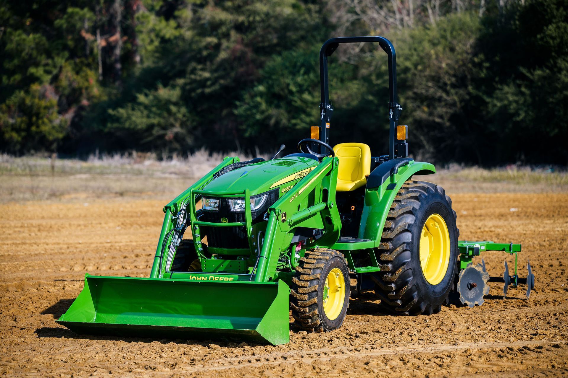 A green john deere tractor is plowing a dirt field.