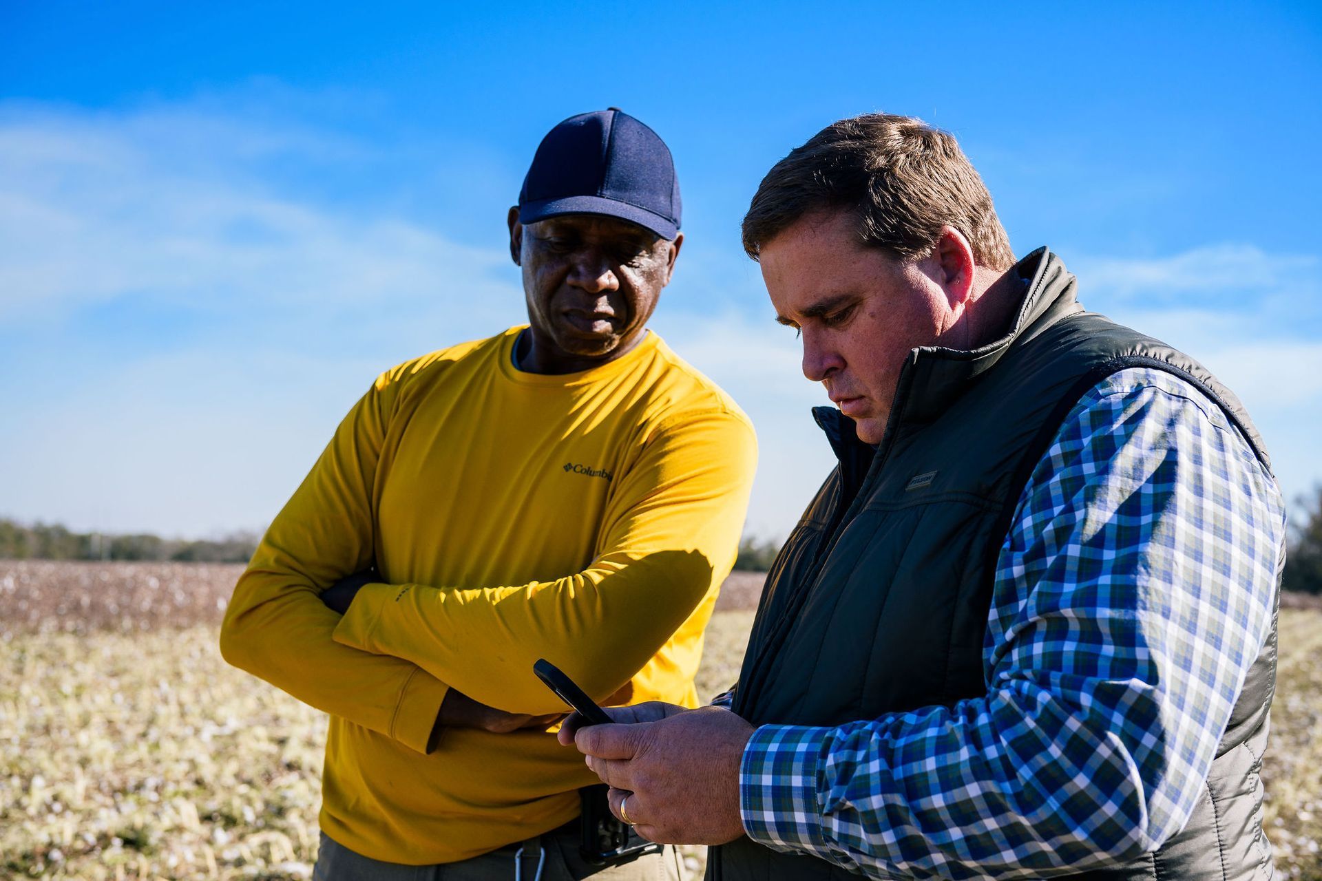 Two men are standing in a field looking at a cell phone.