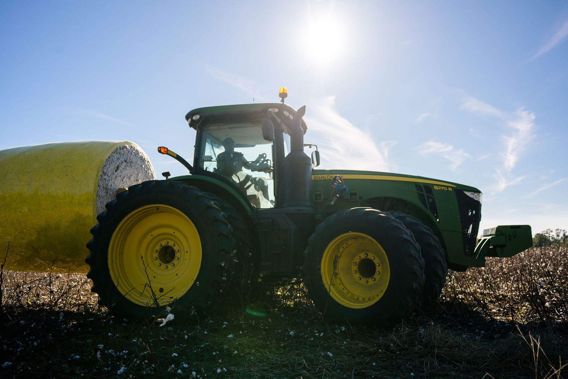 A john deere tractor is carrying a bale in a field.