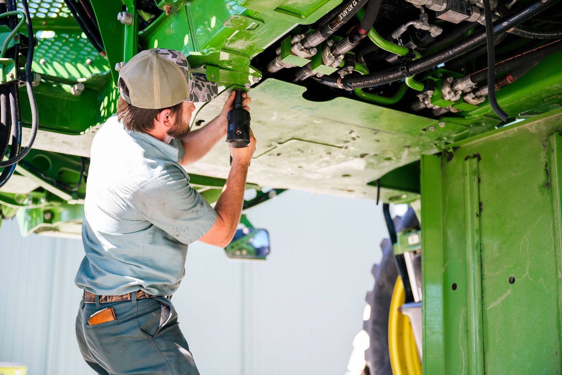 A man is working on a green john deere equipment with a drill.