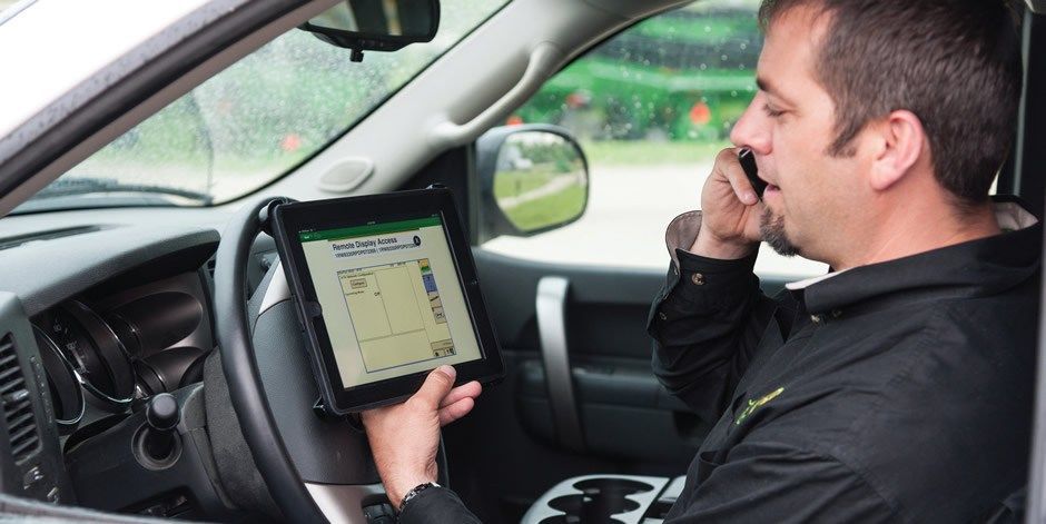 A man is sitting in a car using a tablet and talking on a cell phone.