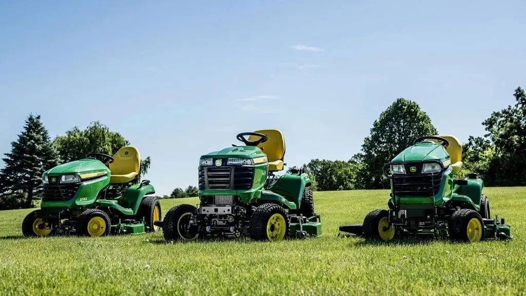 Three john deere lawn mowers are parked in a grassy field.