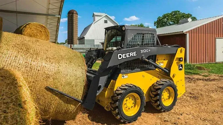 A yellow and black skid steer is loading a bale of hay.