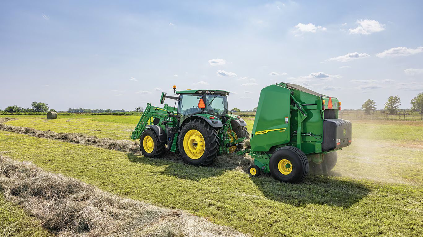 A john deere tractor is baling hay in a field.
