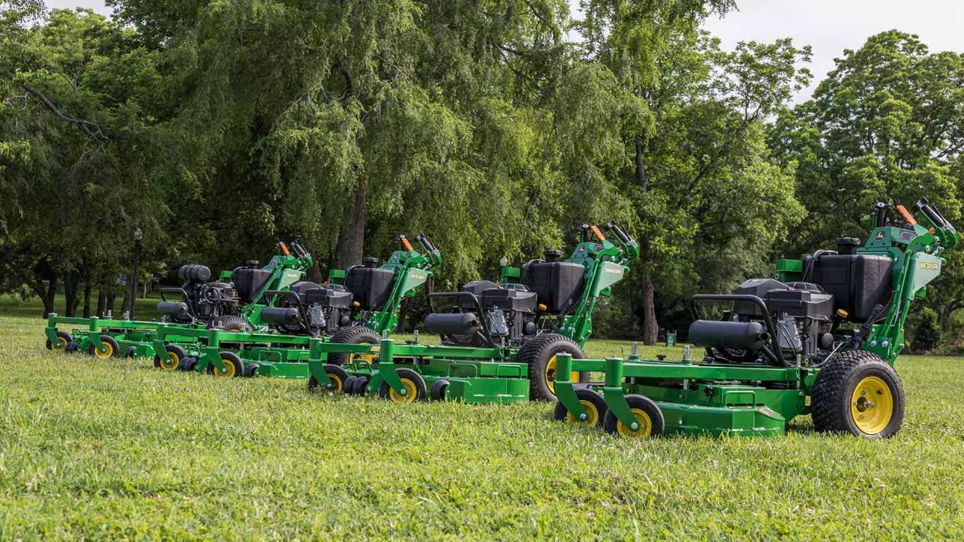 A row of green John Deere mowers are parked in a grassy field.