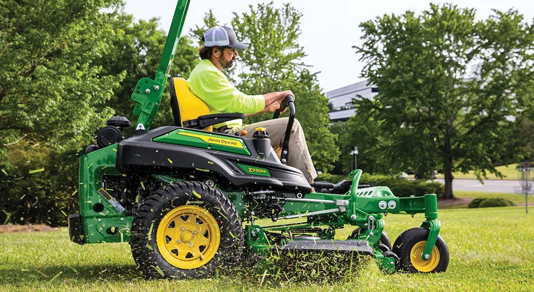 A man is riding a john deere zero turn lawn mower on a lush green lawn.